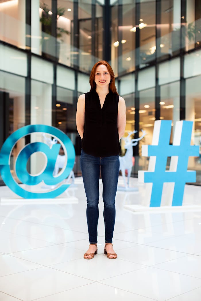About Confident young woman standing in a modern office atrium with digital symbols.